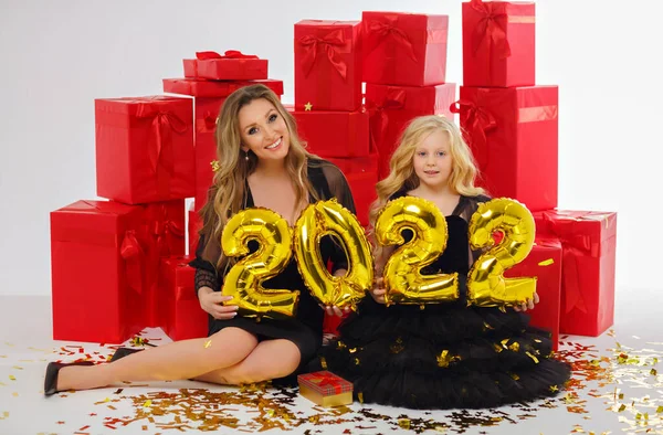 赤の贈り物の背景にある黒のドレスの魅力的なブロンドのお母さんと娘は 新しい年のために 番号2022を保持しています ロイヤリティフリーのストック写真