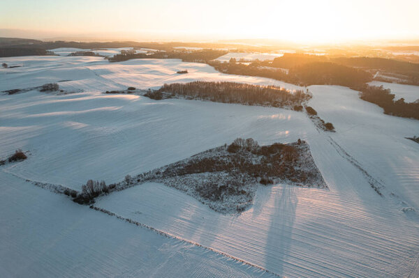 Aerial drone view of winter snow covered fields and forest at sunset