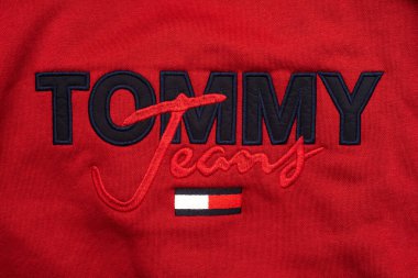 Tekstil desenli kırmızı gömlekli Tommy Hilfiger marka logosu.