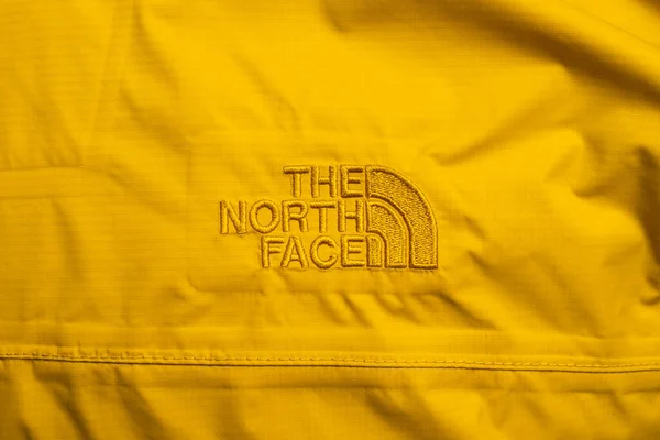Tekstil desenli sarı ceketin üzerinde North Face marka logosu var.