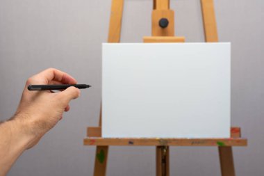 Ahşap sehpadaki boş beyaz tuvali işaret eden kalemle el, yeni fikir, boş alan kavramı, beyaz tahta