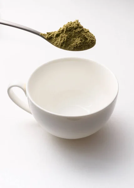 Kratom 'a dikey fotoğraf içirmeye hazır boş beyaz bardağın üzerinde kriatom tozuyla dolu çay kaşığı.