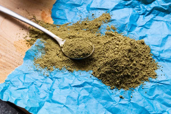 Etrafında çay kaşığı olan mavi kramplı kağıt üzerinde büyük bir yığın yeşil kratom.