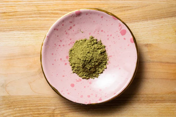 Yeşil kratom tozu yığını küçük bir seramik gül plakası üzerinde tahta desen fotoğraf üst düz yatıyordu