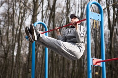 Sakallı hippi yatay barda barfiks çekip karın kaslarını çalıştırıyor.