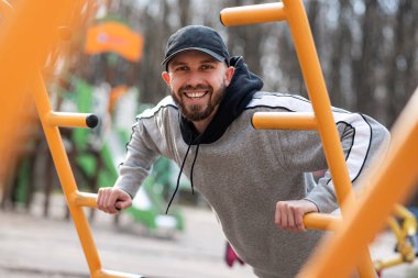 Sakallı genç erkek dışarıda vücut ağırlığı antrenmanı yapıyor spor sahasında şınav çekiyor. 