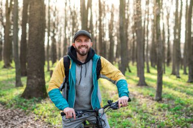 Sakallı mutlu hippi bisikletini güneşli bahar ormanında tutuyor.