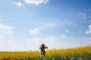 Sarı bir yaz tarlasında şapkalı bir kadın mavi gökyüzü ve bulutlarla özgürlük kavramının önünde duruyor.
