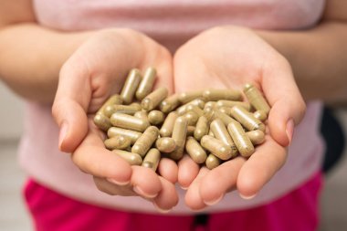 Bir avuç dolusu yeşil kratom hapı kadının ellerinde, yüzü yok, seçici odaklanma