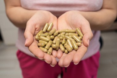 Bir avuç dolusu yeşil kratom hapı kadının ellerinde, yüzü yok, seçici odaklanma