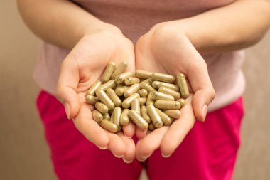 Bir avuç dolusu yeşil kratom hapı kadının ellerinde, yüzü yok, seçici odaklanma