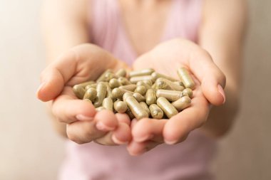 Bir avuç dolusu yeşil kratom hapı kadının ellerinde, yüzü yok, seçici odaklanma