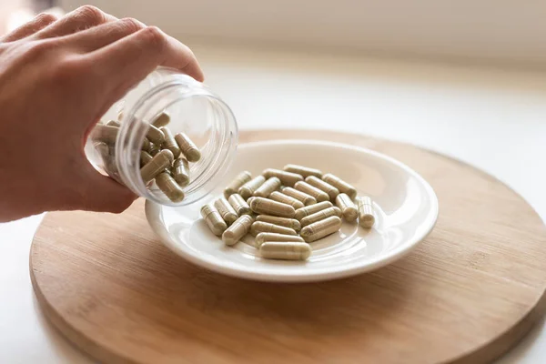 one hand pouring kratom pills out of the glass jar to the white plate, selective focus
