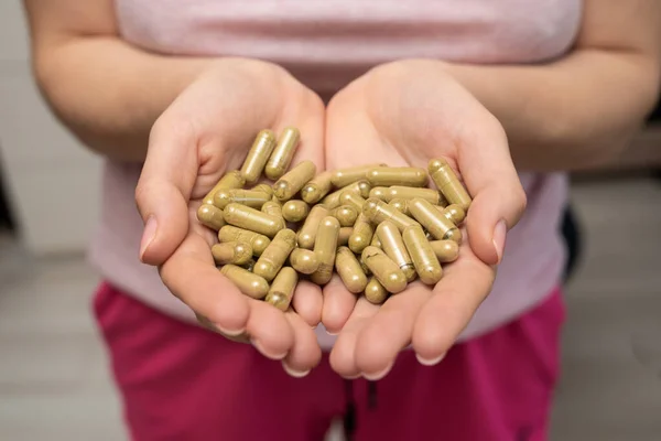 Bir avuç dolusu yeşil kratom hapı kadının ellerinde, yüzü yok, seçici odaklanma