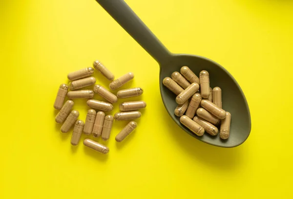 Sarı zemin üzerinde kaşık ve bir avuç dolusu kratom hapı içeren kratom hapları.