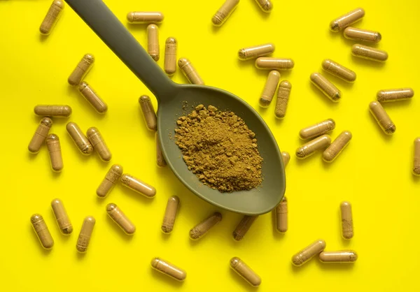 Kratom dolu kaşık ile sarı zemin üzerinde kratom hapları bileşimi, üst görünüm, düz uzanma