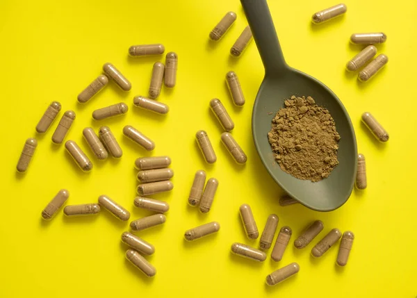 kratom pills composition on yellow background with spoon, handful of kratom pills