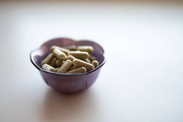 Küçük mor tencerenin içinde bir avuç dolusu yeşil kratom kapsülü, üst görünüm, yüzeysel odak