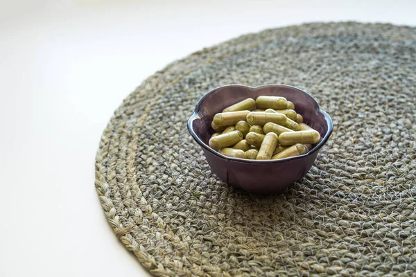 Hasır yüzeydeki küçük mor tencerede bir avuç dolusu yeşil kratom hapı kapsülü