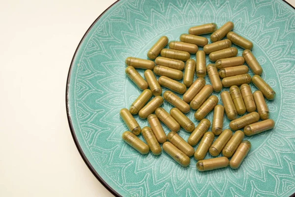 green plate with handful of kratom pills laying randomly, selective focus
