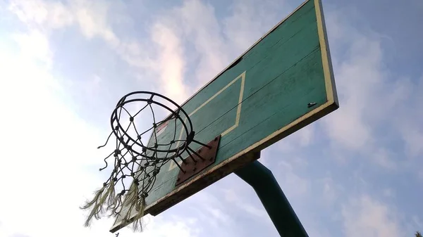 薄緑色の古いバスケットボールのフープと公共のスポーツフィールドで朝の空の青の背景と壊れたネットのフロントバック角度ビュー — ストック写真