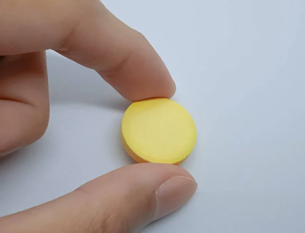 Two fingers of left hand holds a vitamin C tablet, isolated on the white background. Hand holds a vitamin C tablet.