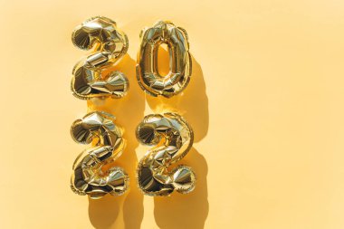 Altın bir zemin üzerinde 2022 rakamları bulunan altın folyodan yapılmış balonlar. Düz yatış, üst görünüm.
