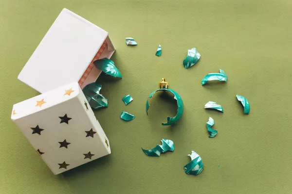 Une boule de jouet cassée sur un fond vert dans un style minimaliste est tombée d'une boîte cadeau. — Photo