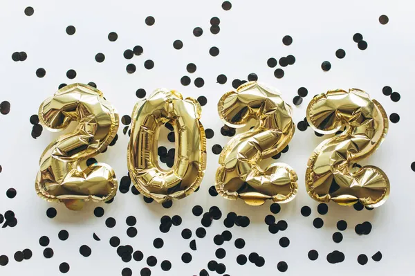 Luftballons aus Goldfolie in Form von Ziffern 2022 mit schwarzem Konfetti auf weißem Hintergrund.. — Stockfoto