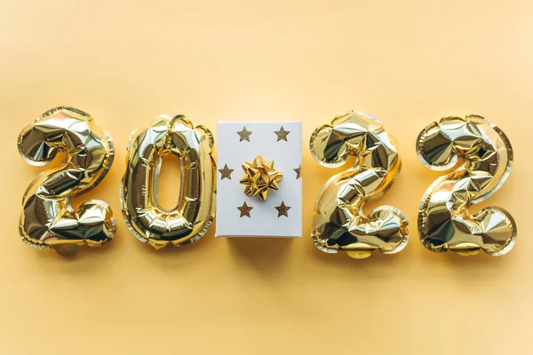 Ballonnen gemaakt van bladgoud in de vorm van nummers 2022 en geschenkdoos op een gouden achtergrond. Kerstmis, Nieuwjaar en feestelijk concept vieren. — Stockfoto