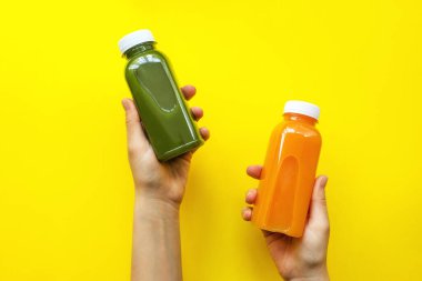 Sarı arka planda meyve suyu veya smoothie ile plastik şişeleri tutan kadın. Diyet konsepti, detoks