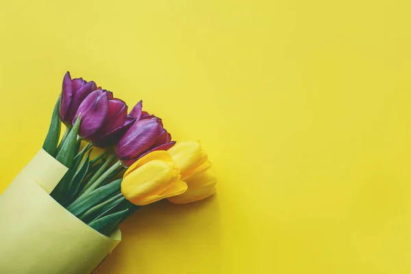 Ramo de hermosos tulipanes morados y amarillos sobre fondo amarillo, vista superior. — Foto de Stock