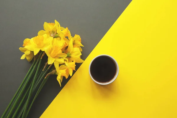 Narcisos amarillos y taza de café sobre fondo amarillo con espacio de copia para texto. — Foto de Stock