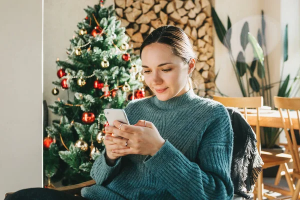 Una joven y hermosa europea usa su teléfono en un ambiente festivo navideño — Foto de Stock