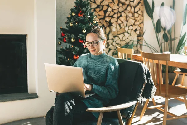 Una joven y hermosa mujer europea utiliza su portátil en casa en un ambiente festivo de Navidad — Foto de Stock