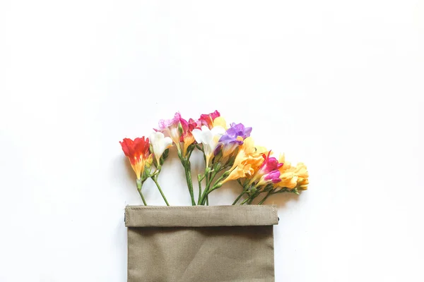 Multicolored freesia flowers and a sprig of cherry blossom in a canvas bag on a white background — стоковое фото