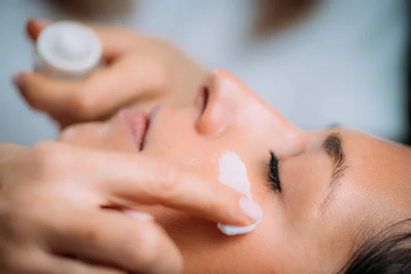 美容师在女人脸上涂乳霜 — 图库照片