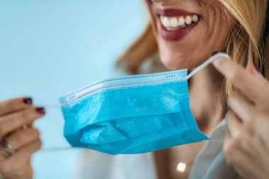 Güzel gülümseyen kadın koruyucu koronavirüs maskesini çıkarıyor.