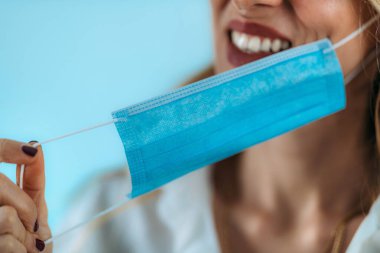 Güzel, gülümseyen bir kadın maskesini suratından çıkarıyor.