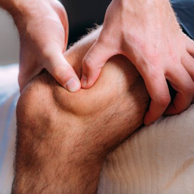 Diz masajı fizyoterapisi. Yaralı dizine fizyoterapist masaj yapıyor. Spor sakatlığı tedavisi.