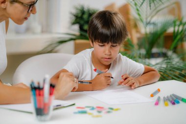 Anaokulu çocuğu okul eğitimi değerlendirme testi yapıyor. Psikolog soru soruyor ve anaokulu çocuğu cevap yazıyor..