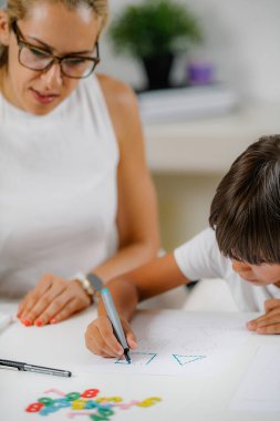 Anaokulu değerlendirme testinde çocuk şekiller çiziyor. Psikolog ona yardım ediyor..