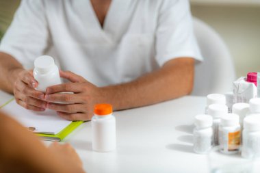 Kuantum Tıbbı. Doctor Holding a Supplement Bottle, bir istemciye ek ürünler öneriyor.