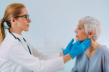Endokrinoloji doktoru tiroid bezi hastalığı belirtileri gösteren yaşlı bir kadını muayene ediyor.