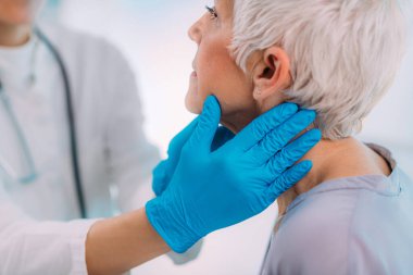 Endokrinoloji doktoru tiroid bezi hastalığı belirtileri gösteren yaşlı bir kadını muayene ediyor.