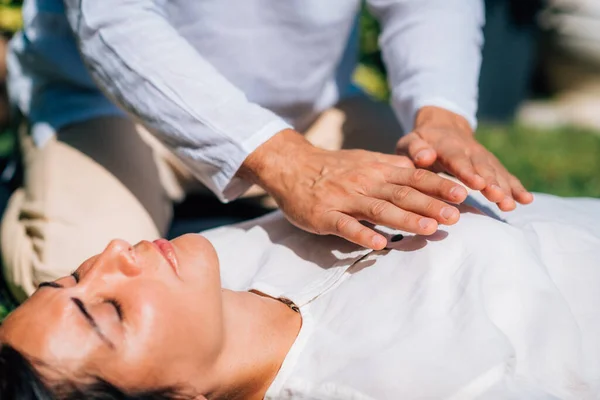 霊気治癒セッションの女性 心臓チャクラの上に手を取り エネルギーを転送レイキセラピスト 平和な女性は彼女の目を閉じて横になっている — ストック写真