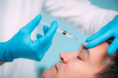 Erkekler için yaşlanma karşıtı tedaviler. Ellerinde cerrahi eldiven var. Deri doldurucu enjekte ediyorlar. Orta yaşlı erkeklerin yüzü...   