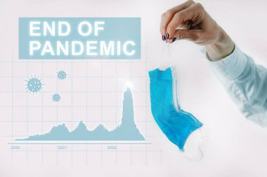 Pandemik kavramsal görüntünün sonu, covid vakalarda azalma, korona virüsü parçacıkları ve buruşmuş koruyucu yüz maskesi tutan bir el gösteren bir grafikle.