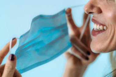 Gülümseyen kadın yüz maskesini çıkarıyor, koronavirüs salgınının sonunu işaret ediyor.