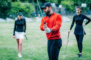 Golf dersi. Golf hocası genç kadınlara salıncak tekniği gösteriyor
